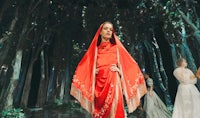 a woman in a red dress walks down a runway in a forest